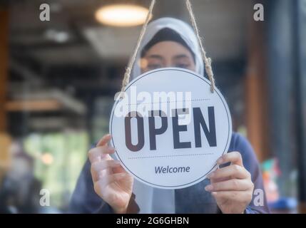 Kaffee-Café-Mitarbeiter, muslimische Angestellte Frau hängen an offenem Schild an der Glastür Stockfoto