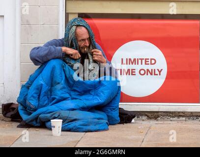 Preston, Lancashire. UK Wetter 6. Juli 2021 Obdachloser Mann in schlechter Gesundheit sitzt auf dem Bürgersteig vor dem Kartengeschäft Verkauf von Weihnachtskarten. Menschen, die Obdachlosigkeit erfahren, insbesondere Menschen, die rauh schlafen, sind während der Pandemie stark gefährdet. Bei ihnen besteht eine dreimal höhere Wahrscheinlichkeit für eine chronische Erkrankung, einschließlich Atemwegserkrankungen wie COPD. Kredit; MediaWorldImages/AlamyLiveNews Stockfoto