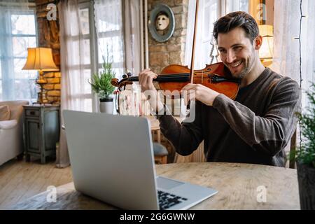 Ein Student lernt online mit einem Laptop Geige spielen. Stockfoto