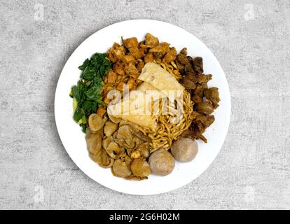 Lecker und lecker Mie ayam oder Mie Yamin oder Yamin Noodle mit Hühnerfleisch, Gemüse, Pangsit Goreng, Pangsit Rebus und Fleischbällchen auf weißem Teller Stockfoto