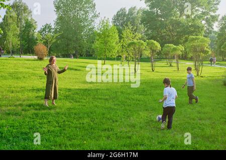 Mutter und zwei Söhne spielen Ball in der Natur, Parkrasen mit Sommerrasen Stockfoto