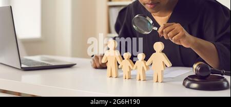 Richter mit Lupe Blick auf hölzerne Familienfiguren stehen auf dem Tisch Stockfoto