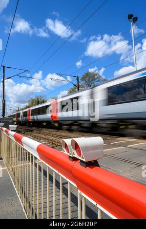 Zug, der in Essex, England, durch einen Bahnübergang mit Geschwindigkeit fährt. Stockfoto