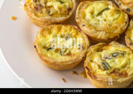 Teller mit Mini-Quiche mit Speck und Kräutern - Mini-Bohnenkuchen auf weiß mit Kopierfläche Stockfoto