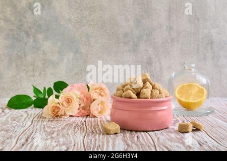 Brauner Zucker in einer Keramikschale, Rosen und Zitrone auf einem Holztisch, Stillleben Stockfoto