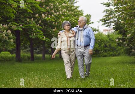 Ältere Männer und Frauen gehen auf grünem Gras im Park zwischen den Bäumen. Stockfoto