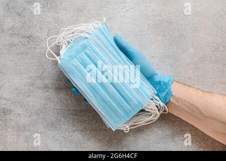 Mans Hand in einem chirurgischen Handschuh hält einen Stapel von medizinischen Einwegmasken Stockfoto