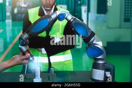 Asiatische Ingenieure männlich weiblich in der Industrie tragen Harthüte in der Industrie Fertigung Fabrik mechanische Anzeige Schnittstelle Arm Roboter Fertigung indust Stockfoto