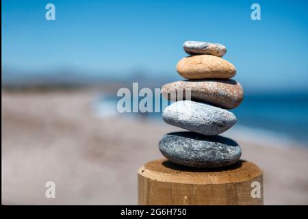 Gleichgewicht und Schönheit in einer pyramidenförmigen Form von fünf Steinen, die übereinander in Balance gebracht werden, mit Blick auf das Meer, was Frieden und visuelle Harmonie gibt. Stockfoto