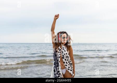 Glückliche junge schöne afro amerikanische Frau lächelnd, trägt Kopfhörer tanzen und heben Arm am Strand.Frau genießen Sommerferien Konzept li Stockfoto
