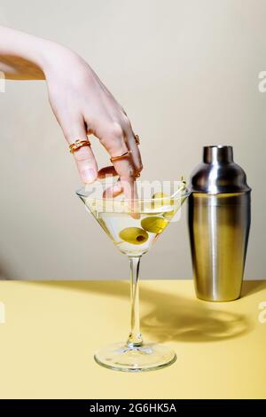 Frau taucht Finger mit Ringen in ein Glas martini-Cocktail mit Oliven Stockfoto