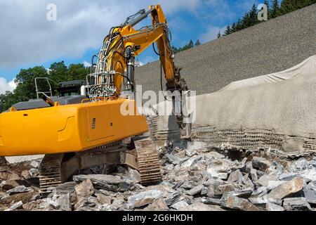 Bagger mit hydraulischen Hammermeißeln Stein. Autobahnbaustelle am Hang. Der Damm wird gesichert. Wand mit Beton und Verstärkung Stockfoto