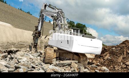 Ein weißer Bagger bietet Platz für eigenen Text. Er meißelt Steine mit einem hydraulischen Hammer. Autobahnbaustelle am Hang. Wand mit Beton und reba Stockfoto