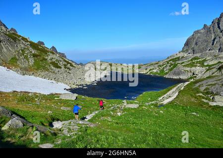 Der Bergsee Starolesnianske pleso am oberen Ende der Schlucht Velka Studena Dolina in der Hohen Tatra. Zwei Wanderer auf einem Wanderweg. Slowakei. Stockfoto