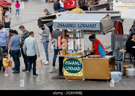 Street Food Stand und Verkäufer, die osmanisches Dessert servieren und verkaufen, Hefe-Krapfen in dickem Sirup. Menschenmenge auf dem Eminonu-Platz in Istanbul, Türkei. Stockfoto