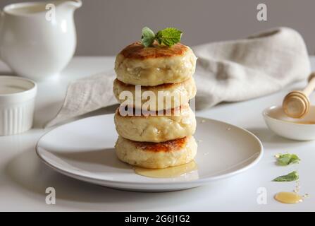 Süße Käsepfannkuchen mit Honig auf einem weißen Teller. Hausgemachte Käsekuchen mit Rezept. Stockfoto