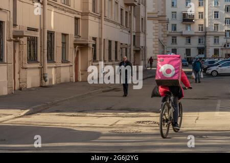 Lebensmittelzustellung Mann auf einem Fahrrad mit rosa gebrandeten Rucksack Reiten Fahrrad im Hof, Rückansicht, St. Petersburg, Russland. Stockfoto