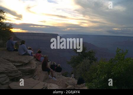 Menschen, die auf einem Felsvorsprung am Südrand des Grand Canyon sitzen und den Sonnenuntergang genießen Stockfoto