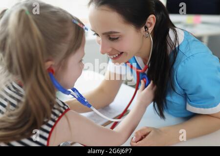 Arzt hört dem kleinen Mädchen mit Stethoskop zu und spielt mit ihr in der Klinik Stockfoto