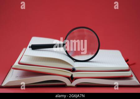 Lupe, die auf Bücherhaufen auf rotem Hintergrund liegt, Nahaufnahme Stockfoto