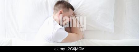 Der junge Mann schläft friedlich auf dem großen weißen Bett Stockfoto