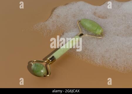 Grüne Jade Gesichtswalze liegt im Schaum. Hautpflegewerkzeuge. Beauty Roller für bessere Durchblutung und Muskelaktivierung. Stockfoto