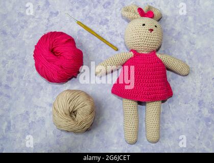 Rosa und beige Strickwolle, Kaninchen-Amigurumi und Häkelhaken auf blauem pastellfarbenem Hintergrund.Amigurumi Stufen.Draufsicht.Handgestrickte Spielzeug. Amigurumi. Stockfoto