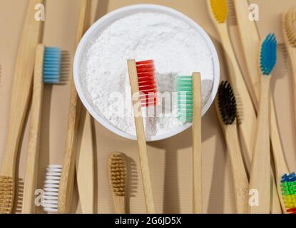 Ein Set aus bunten, umweltfreundlichen Bambuszahnbürsten und weißem Zahnpulver auf einem beigefarbenen, pastellfarbenen Hintergrund. Abfallfreie, nachhaltige Lebensweise. Kunststoff Stockfoto