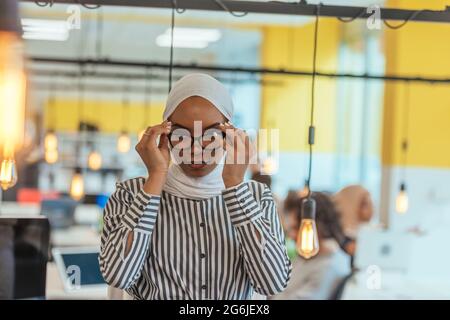 Trait einer schwarzen (afroamerikanischen) weiblichen muslimin, die in einem modernen Geschäftsbüro steht, während sie einen Hijab trägt. Stockfoto