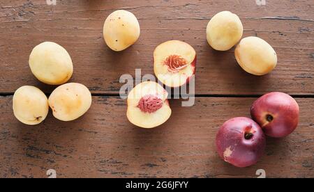 Obst auf einem rustikalen Tisch. Reife gelbe und rote Pfirsiche liegen auf einem Holztisch, auf dem Tisch LIEGT EIN in zwei Hälften geschnittener Pfirsich Stockfoto