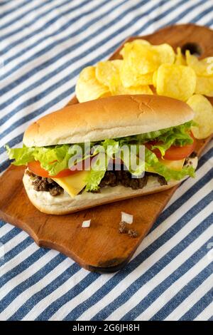 Hausgemachtes, gehacktes Rindfleisch-Sandwich mit Kartoffelchips auf einem rustikalen Holzbrett, Seitenansicht. Stockfoto