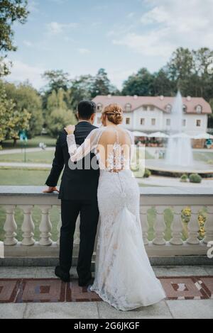 Junge Braut und Bräutigam auf einem Balkon, der für das Fotoshooting zur Hochzeit posiert Stockfoto