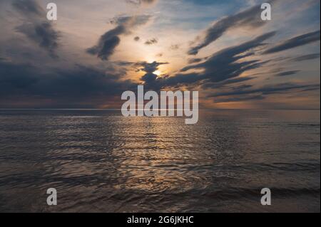 Sonnenuntergang im Meer mit Wolken und ruhigem Wasser auf dessen Oberfläche Sonnenlicht reflektiert, indem es einen Lichtweg schafft Stockfoto