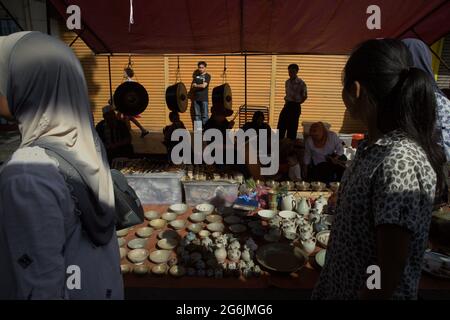 Menschen, die die Gaya Street entlang gehen, vorbei an einem Händler von Porzellan, Gongs und Antiquitäten während des Gaya-Sonntagsmarktes. Kota Kinabalu, Sabah, Malaysia. Stockfoto