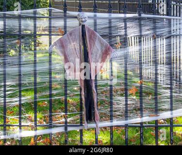 Halloween Zombie Dekoration auf Eisenzaun mit dekorativem Spinnennetz und Herbstblättern rundherum durch Sonnenschein und Schatten hervorgehoben Stockfoto