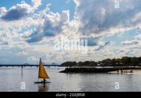 Singlehander segelt Dinghie in der Dämmerung mit Brücke und Bergen in der Ferne unter dramatischem Himmel - Bribie Island Australia Stockfoto