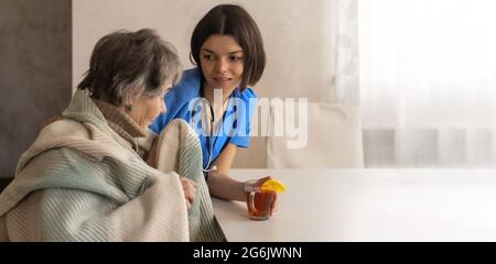 Der Arzt brachte heißen Zitronentee und sitzt mit der Patientin, eingewickelt in eine Decke, wenn sie eine Erkältung hat. Stockfoto