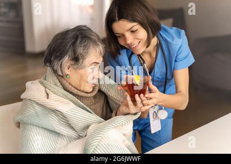 Der Arzt brachte heißen Zitronentee und sitzt mit der Patientin, eingewickelt in eine Decke, wenn sie eine Erkältung hat. Stockfoto