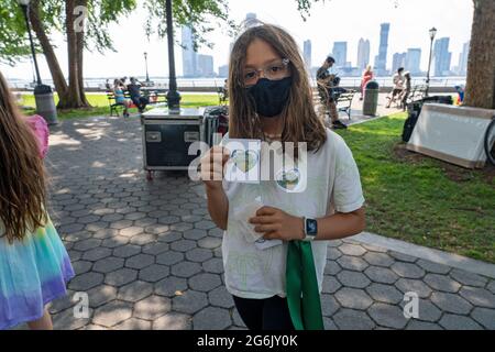 NEW YORK, NY – 05. JULI: Ein Kind gibt Aufkleber und grüne Bänder während einer Kundgebung im Rockefeller Park aus Protest gegen die Gouverneur aus. Andrew Cuomos Pläne für ein COV Stockfoto