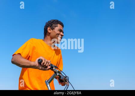 Afroamerikanischer Mann sitzt auf dem Fahrrad draußen vor blauem Himmel Hintergrund Stockfoto