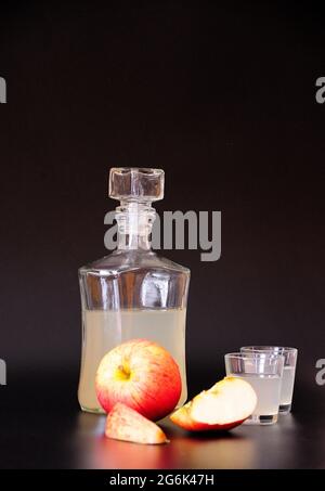 Eine Flasche und zwei Gläser mit hausgemachten Calvados, reife Äpfel in der Nähe auf schwarzem Hintergrund. Nahaufnahme. Stockfoto