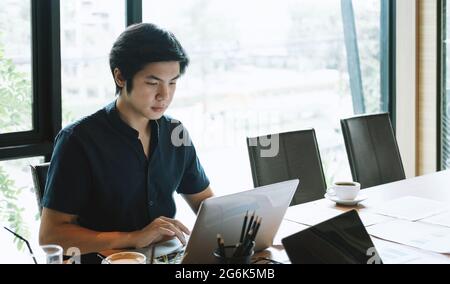 Junger asiatischer Mann, der zu Hause mit einem Laptop arbeitet. Geschäftsfinanzkonzept Stockfoto