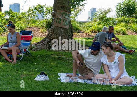 Während eines Protestes gegen die Pläne des Gouverneurs Andrew Cuomo für ein COVID-19-Denkmal in New York City ruhen die Menschen im Schatten eines Baumes.zweihundert Demonstranten versammelten sich im Rockefeller Park in Lower Manhattan, um den Druck auf den Gouverneur aufrecht zu erhalten Andrew Cuomo, nur wenige Tage nachdem der mächtige und skandalös vernarbte Staatschef seine Pläne vernickt hatte, einen Teil der Grünfläche für das Coronavirus-Denkmal, das „Heldenkreis“-Denkmal, zu pflastern. Der Protest in Battery Park City ereignete sich, als das Gemeinderegium 1, das das Gebiet vertritt, ein Treffen am Mittwoch anberaumt Stockfoto