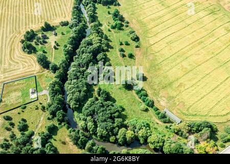 Luftaufnahme der ländlichen Gegend mit Bauernhöfen und gewundenen kleinen Fluss zwischen grünen Bäumen in sonnigen Sommertag Stockfoto