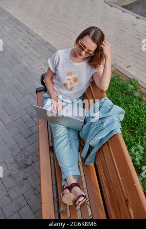 In einem Anzug arbeitet das Mädchen auf einer Bank auf einem Laptop Stockfoto