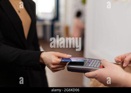 Nahaufnahme einer Geschäftsfrau, die eine Plastikkreditkarte in der Hand hält und im Büro des Unternehmens für die Lieferung von Lebensmitteln bezahlt. Mit kontaktlosem Pay für Essen zum Mitnehmen. Bringen Sie leckeres Essen mit. Stockfoto