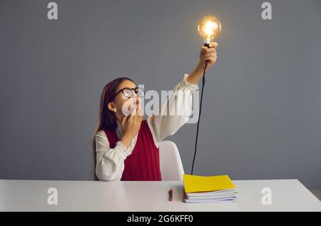 Grundschüler sitzen am Schreibtisch und schauen überrascht auf die leuchtende Glühbirne Stockfoto