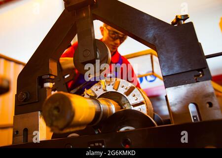 Atyrau, Kasachstan - Mai 21,2012: Arbeiter (Gesicht unscharf) in Schutzbrille und rotem T-Shirt stellt elektrischen Motorrotor wieder her (Nahaufnahme, im Fokus). Stockfoto