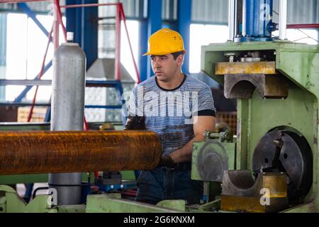 Region Almaty, Kasachstan-Juni 06,2012: INDUSTRIEGEBIET DAMU, Werk Sonik. Drehmaschine (Wender) macht Facette auf verrosteten Rohren. Grüne Maschine, yello Stockfoto
