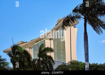 Seitenansicht des Teils Marina Bay Sands hinter Palmen, klarer blauer Himmel, Singapur. Ikonisches Wahrzeichen und Haupttouristenattraktion Stockfoto